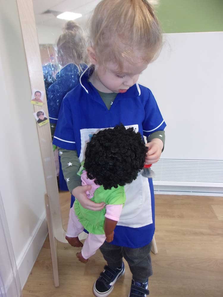 A preschool child dressed up as a nurse cares for a baby doll.